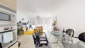 Eine moderne Küche mit Einbauofen, Mikrowelle und einem großen Fenster. Es gibt einen Essbereich mit einem Glastisch und Stühlen sowie einen gelben Teppich.