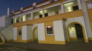 En bygning med flere etager, en gul og hvid facade, flere altaner og en trappe til indgangen.