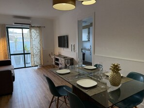 Uma área de refeições moderna com mesa de vidro, cadeiras e televisão acima.