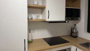 Une cuisine moderne avec des meubles blancs, un plan de travail noir et un téléviseur encastré au-dessus de la cuisinière.