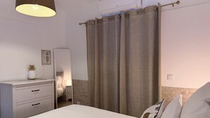 Une chambre à coucher avec un lit, une table de chevet, une lampe, un miroir et un rideau.