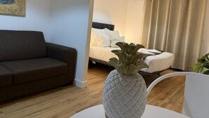 A modern living room with a sofa, a bed with white bedding, a pineapple-shaped vase, and a hanging light fixture.