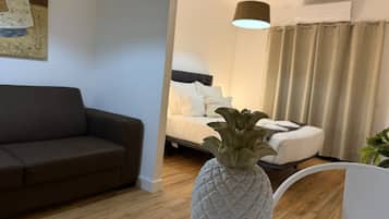 Ett modernt vardagsrum med en soffa, en säng med vita sängkläder, en vas formad som en ananas och en hängande lampa.