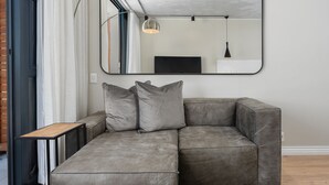 A gray sectional sofa with three cushions, a small wooden side table, and a large mirror on the wall. - Docklands 409 (Cape Town)