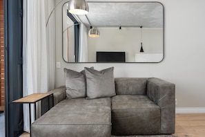 A gray sectional sofa with three cushions, a small wooden side table, and a large mirror on the wall.