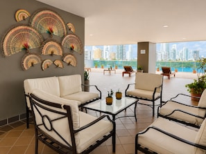 Ein moderner Lounge-Bereich mit einer Couch, Sesseln und einem Couchtisch, mit Blick auf eine Stadtansicht durch große Fenster.