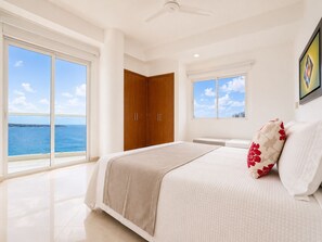 A bedroom with a large bed, a window with a city view, and a door leading to another room.