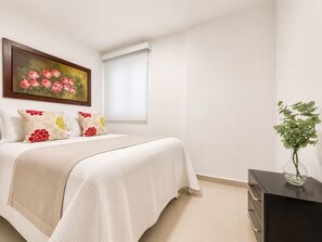 Una camera da letto con un letto, un quadro di fiori, una finestra e un vaso con piante verdi.