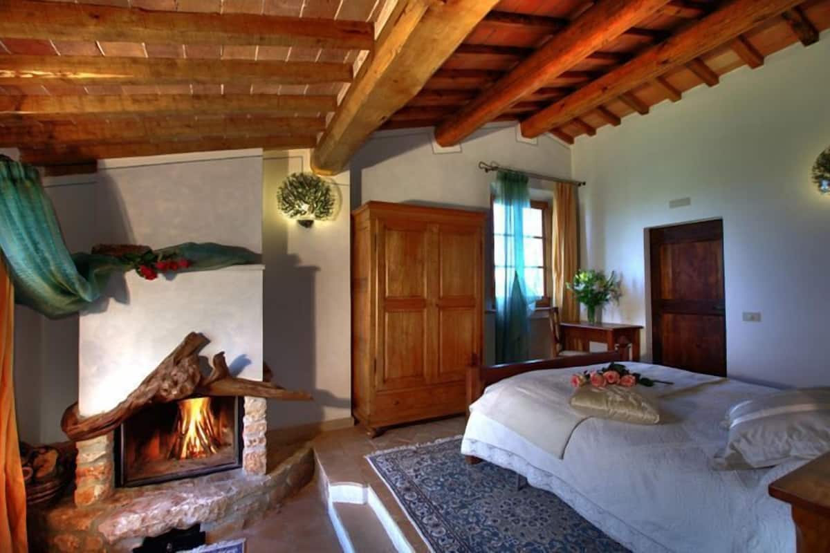 Um quarto aconchegante com lareira de pedra, guarda-roupa de madeira e cama com almofadas florais.