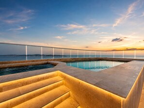 A pool area with a glass balustrade, a set of stairs, and a sunset view.