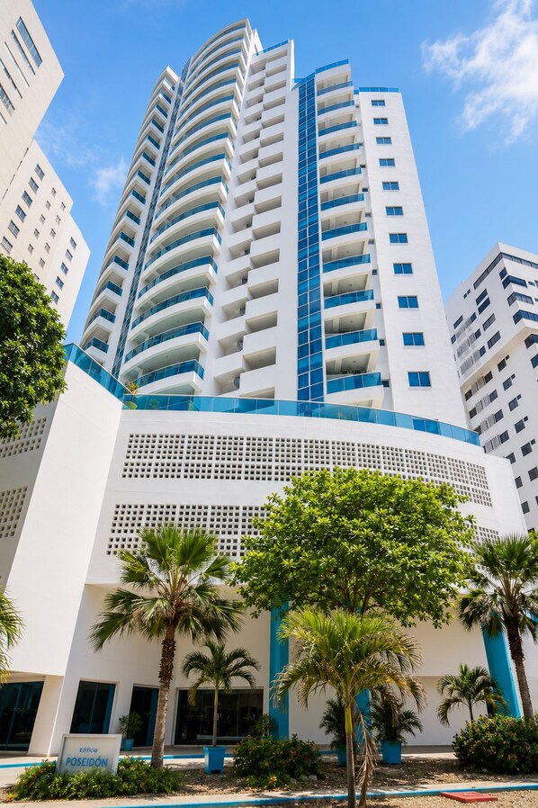 Un immeuble moderne de grande hauteur, doté de nombreux balcons et entouré de palmiers et d’autres plantes.