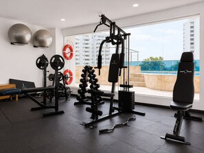 A modern gym with various exercise equipment, a bench, and a view of a swimming pool through large windows. - Penthouse • Private pool • Ocean view • Beach 1803 (Cartagena)