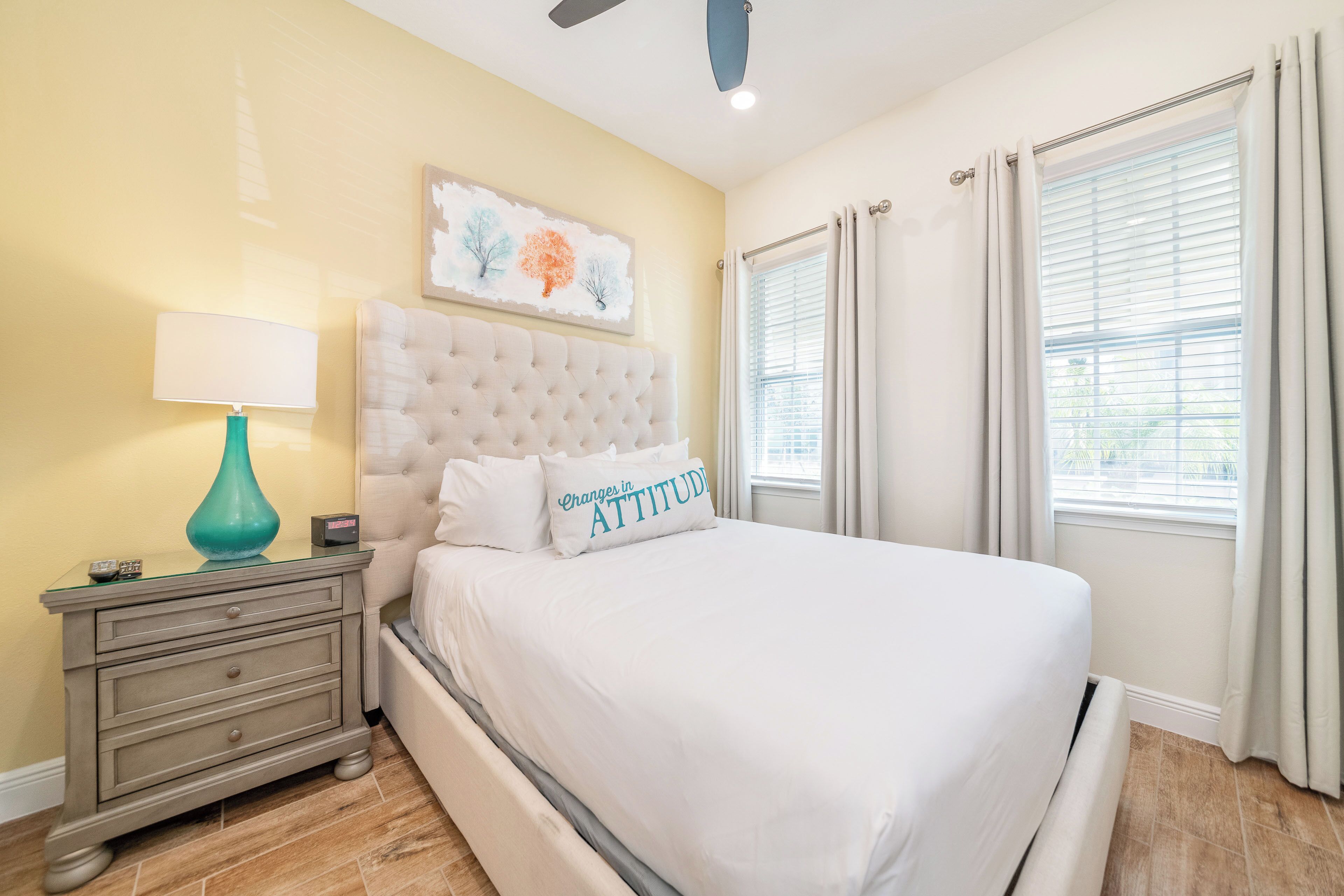 A bedroom with a tufted headboard, a bedside table with a lamp, and a bed with white bedding.