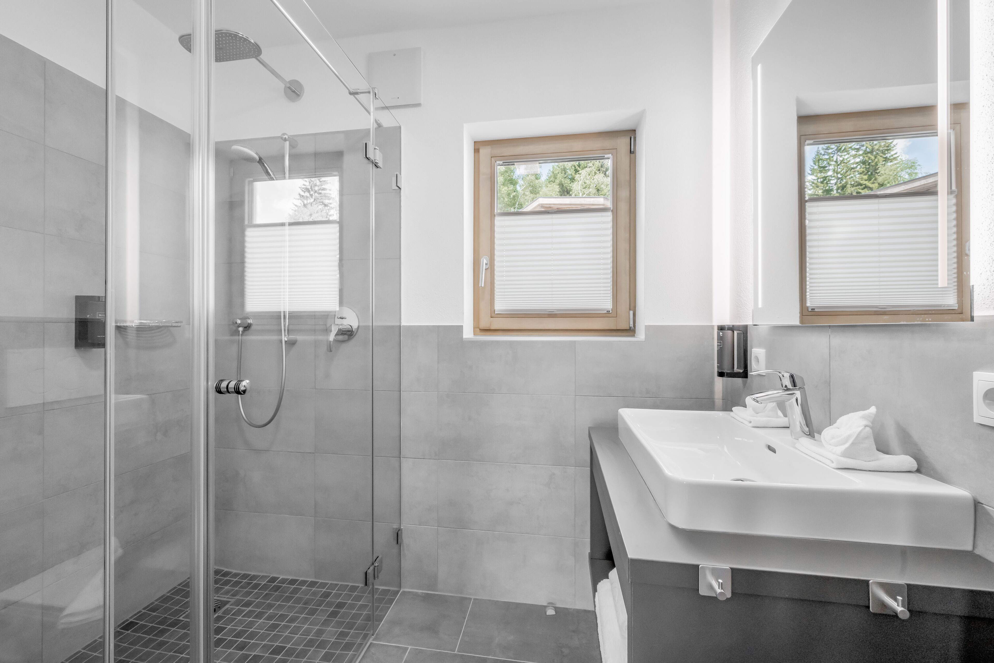 Un bagno moderno con doccia vetrata, un lavandino spazioso e due finestre con stipiti in legno.