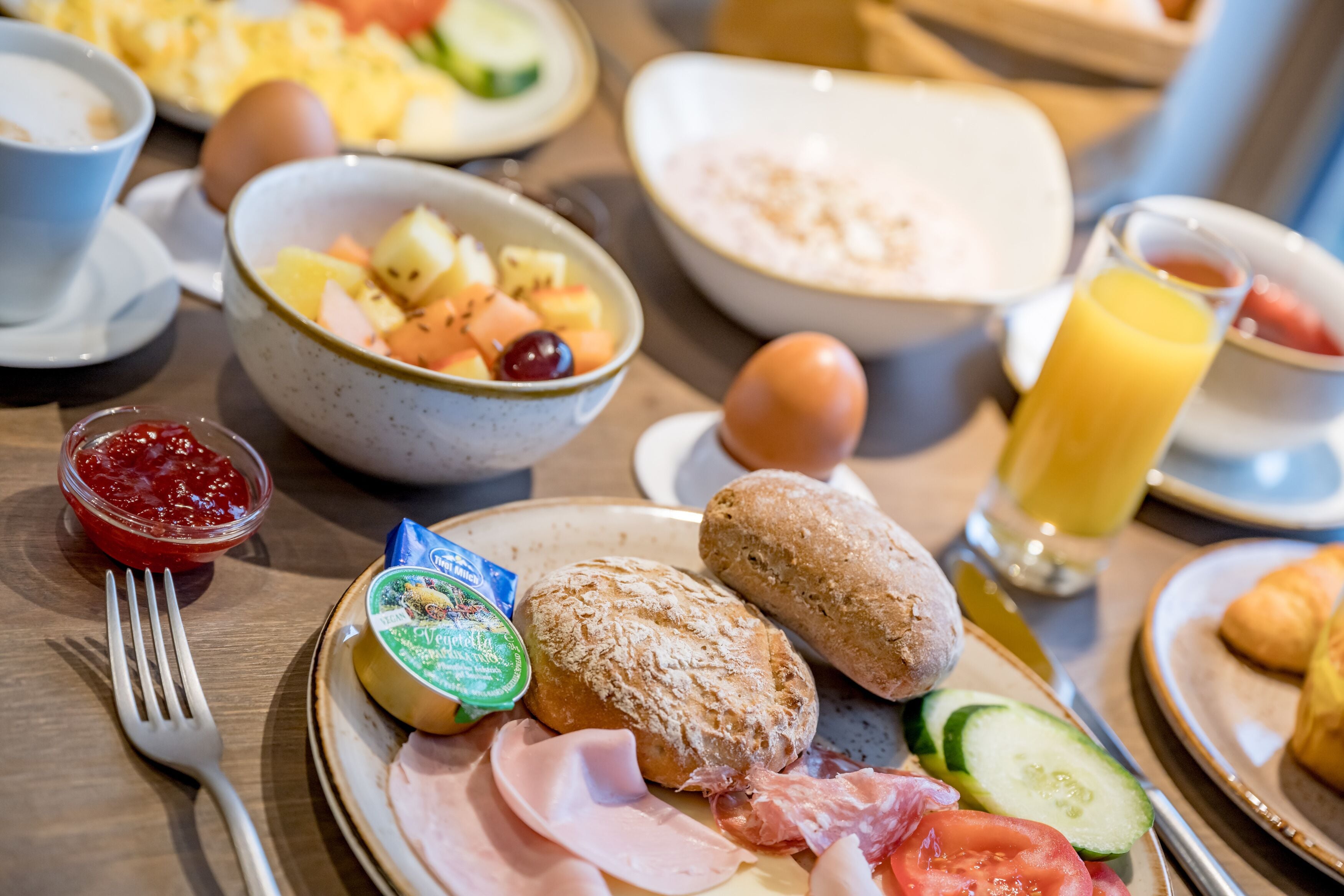 A breakfast table with various food items including eggs, bread, cheese, and fruit.