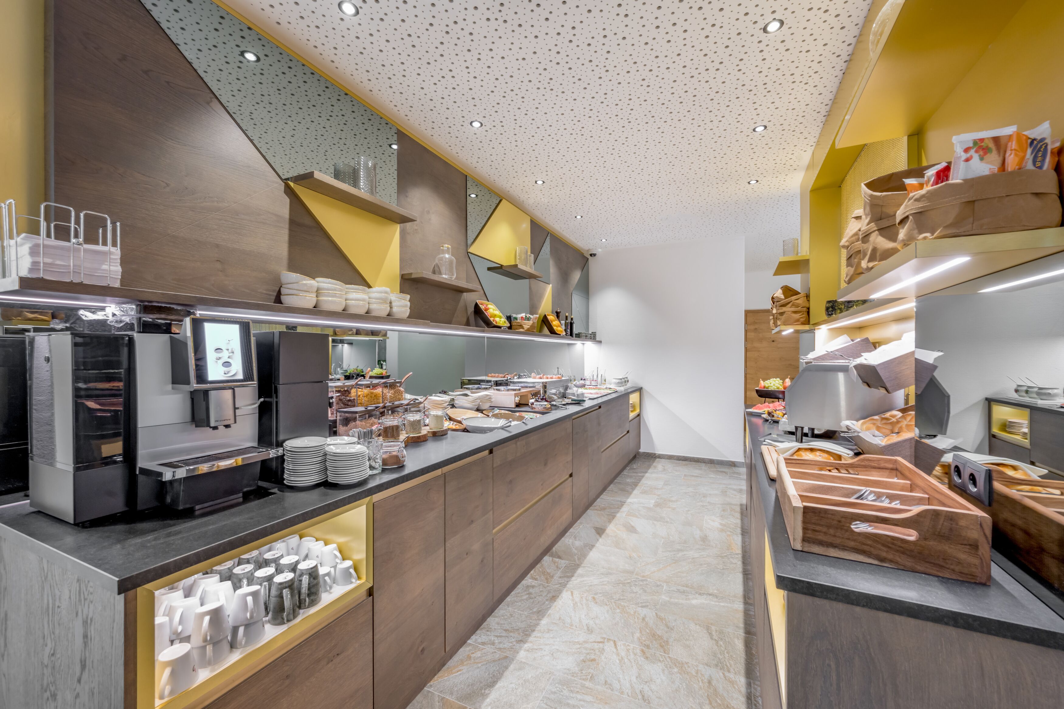 Cozinha moderna com bancada comprida, máquinas de café e diversos alimentos.