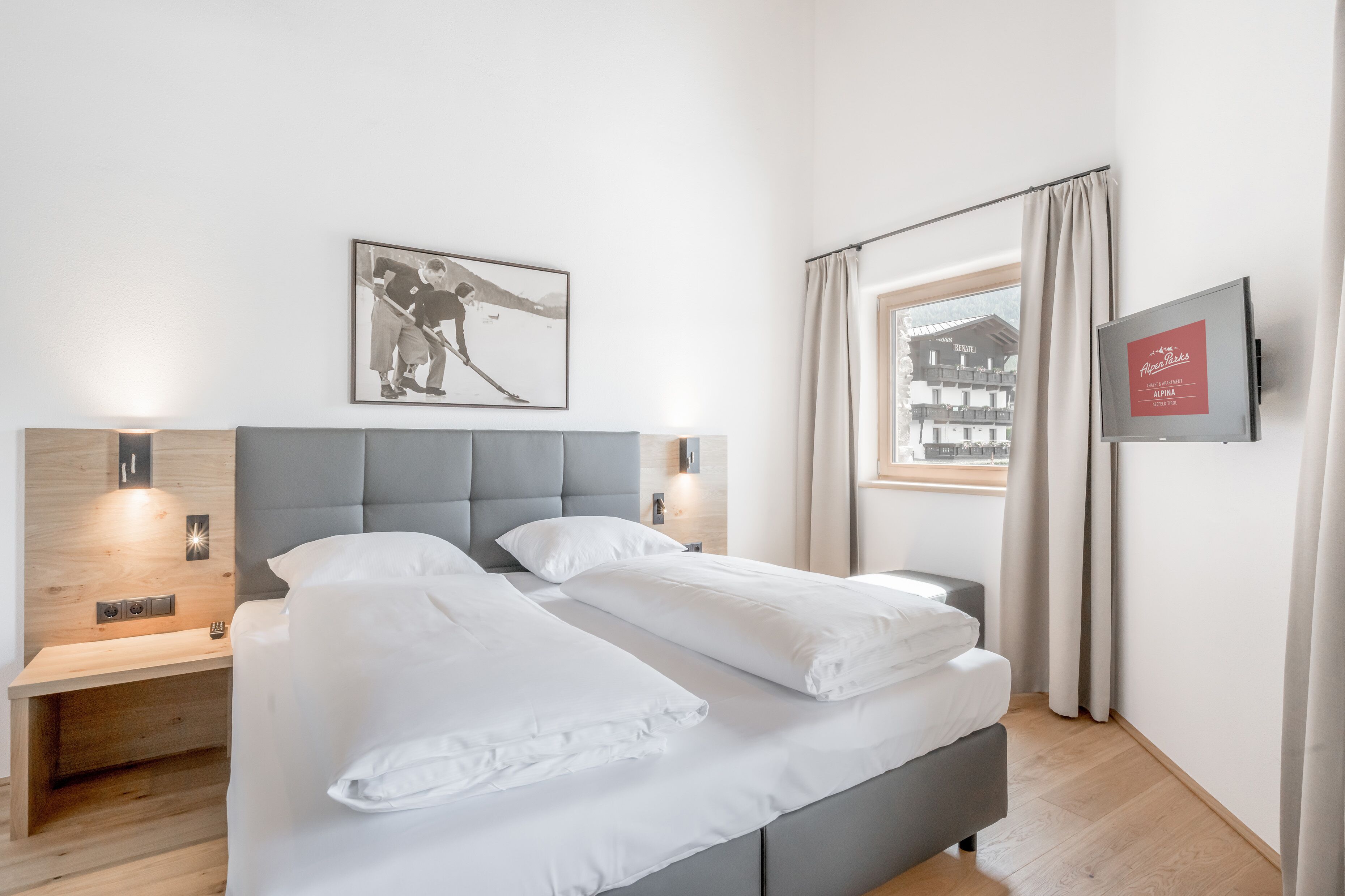 Een hotelkamer met een bed, nachtkastje, wandtelevisie en een raam met gordijnen.