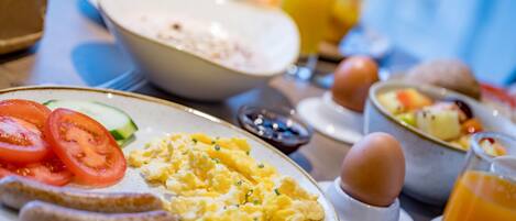 Una mesa de desayuno con huevos revueltos, salchichas, tomates y un tazón de cereal.