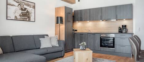 A modern living room with a grey sofa, a small wooden side table, and a plaid ottoman.
