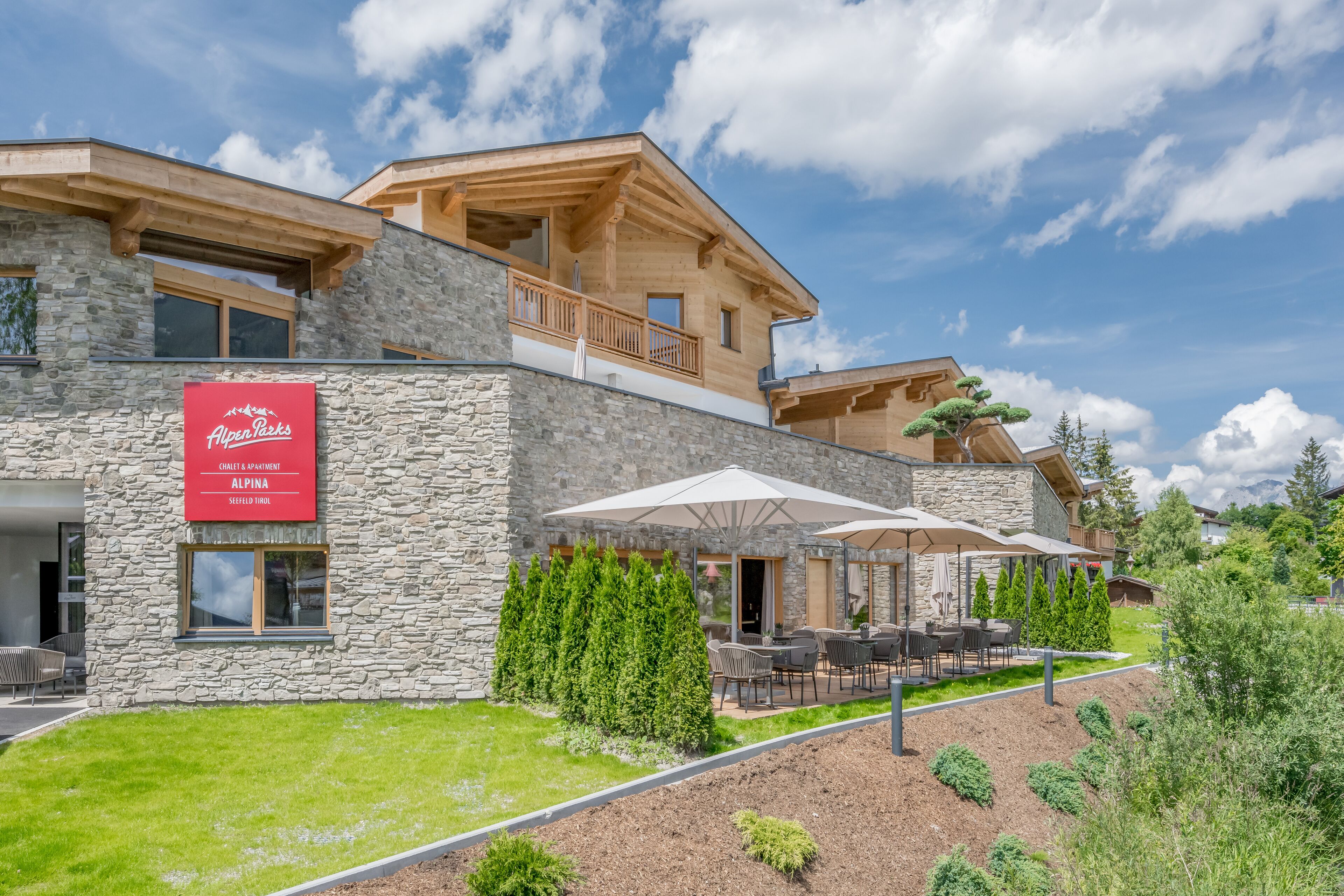 A modern hotel with stone facade, outdoor seating, and a sign for 'Alpen Peaks'.