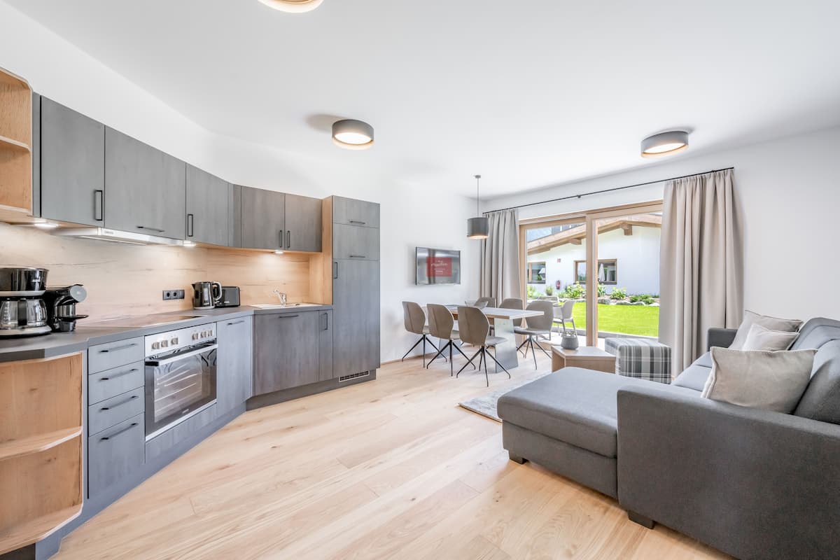 A modern kitchen with grey cabinets, a built-in oven, and a dining area with a grey sofa and table.