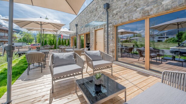 An outdoor patio with wooden flooring, cushioned seating, and large umbrellas. - AlpenParks Chalet & Apartment Alpina Seefeld (Seefeld in Tirol)