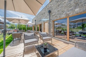 An outdoor patio with wooden flooring, cushioned seating, and large umbrellas. - AlpenParks Chalet & Apartment Alpina Seefeld (Seefeld in Tirol)