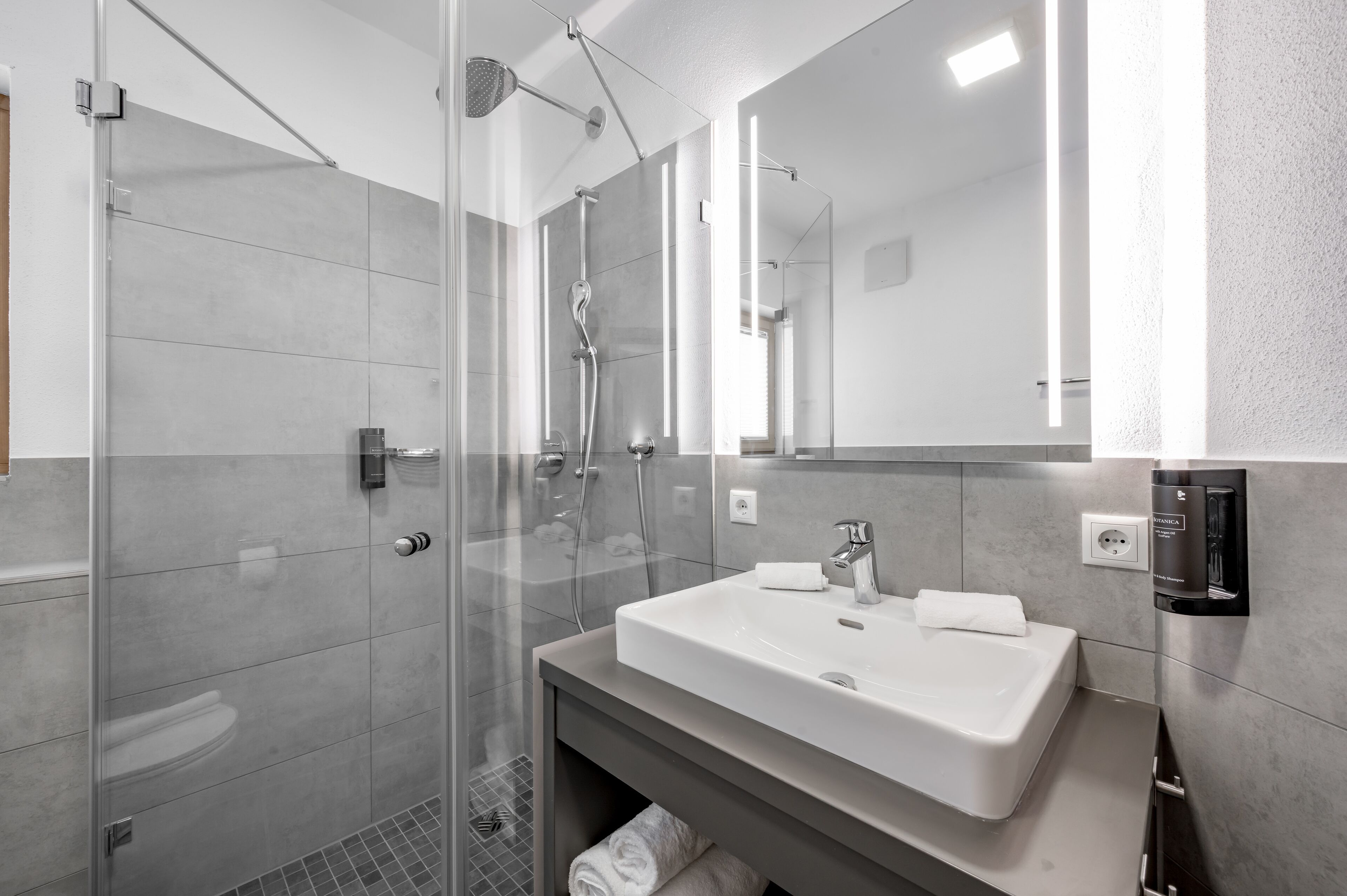A modern bathroom with a glass-enclosed shower, a white sink, and a large mirror.