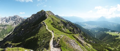 Un sendero de montaña con excursionistas, rodeado de exuberantes valles verdes y montañas lejanas.