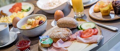 A breakfast buffet with various dishes including eggs, bread, fruits, and meats.