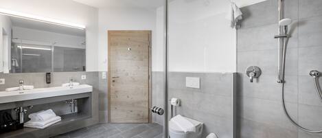 A modern bathroom with a glass shower enclosure, a wooden door, and a vanity with a mirror and towel rack.