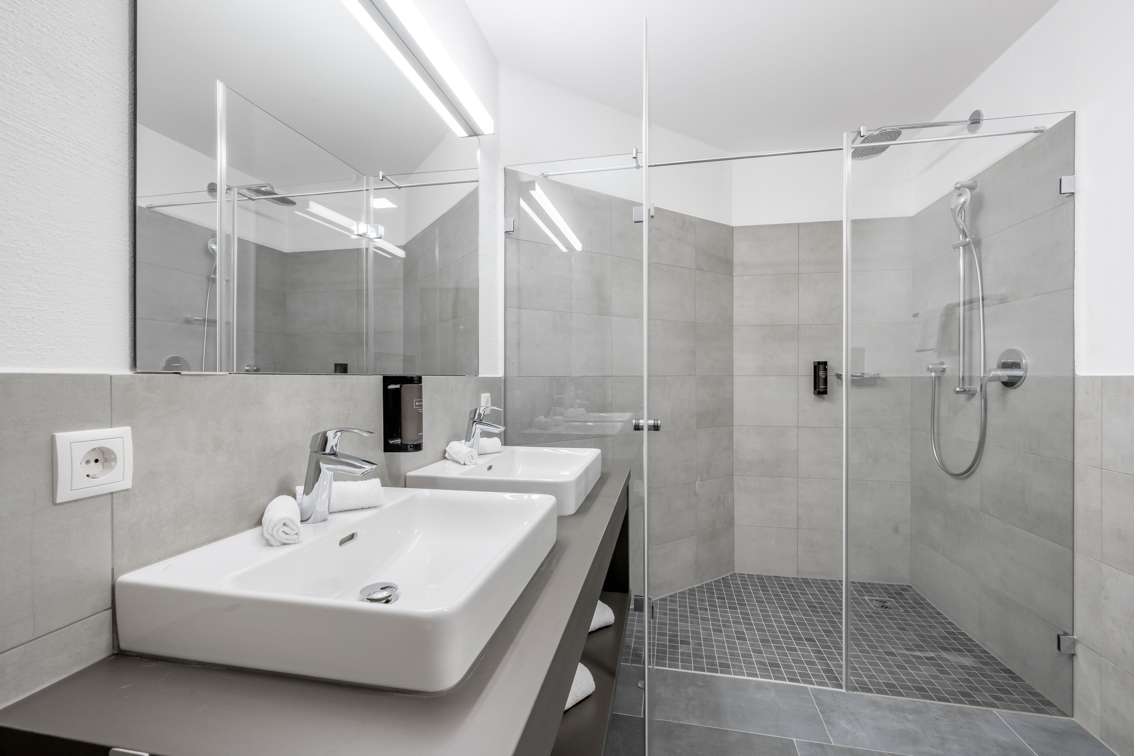 Ein modernes Badezimmer mit zwei Waschbecken, einer Duschkabine aus Glas und einem großen Spiegel.