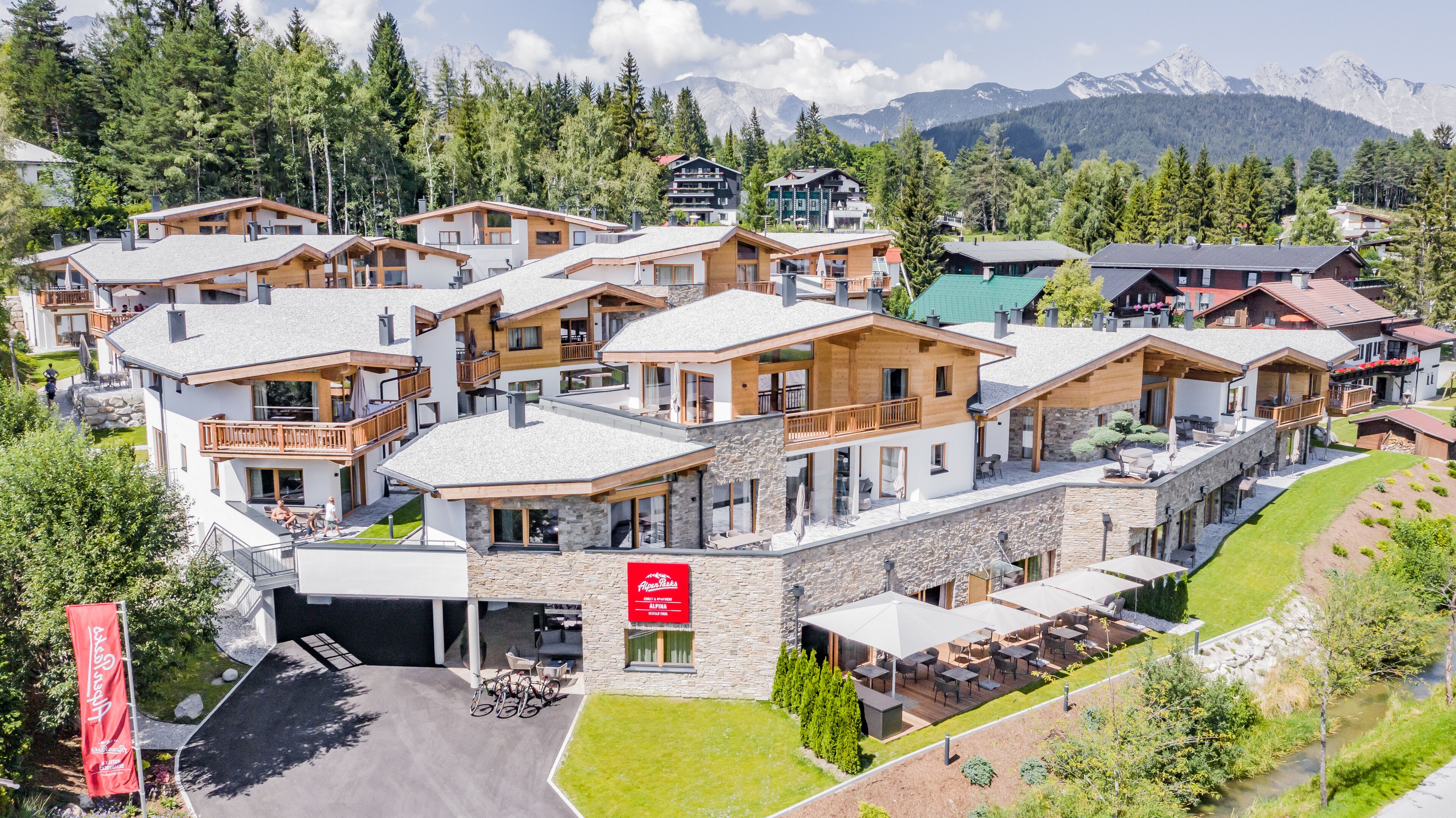 Een modern skigebied met meerdere chalets, terrassen en een berg op de achtergrond.