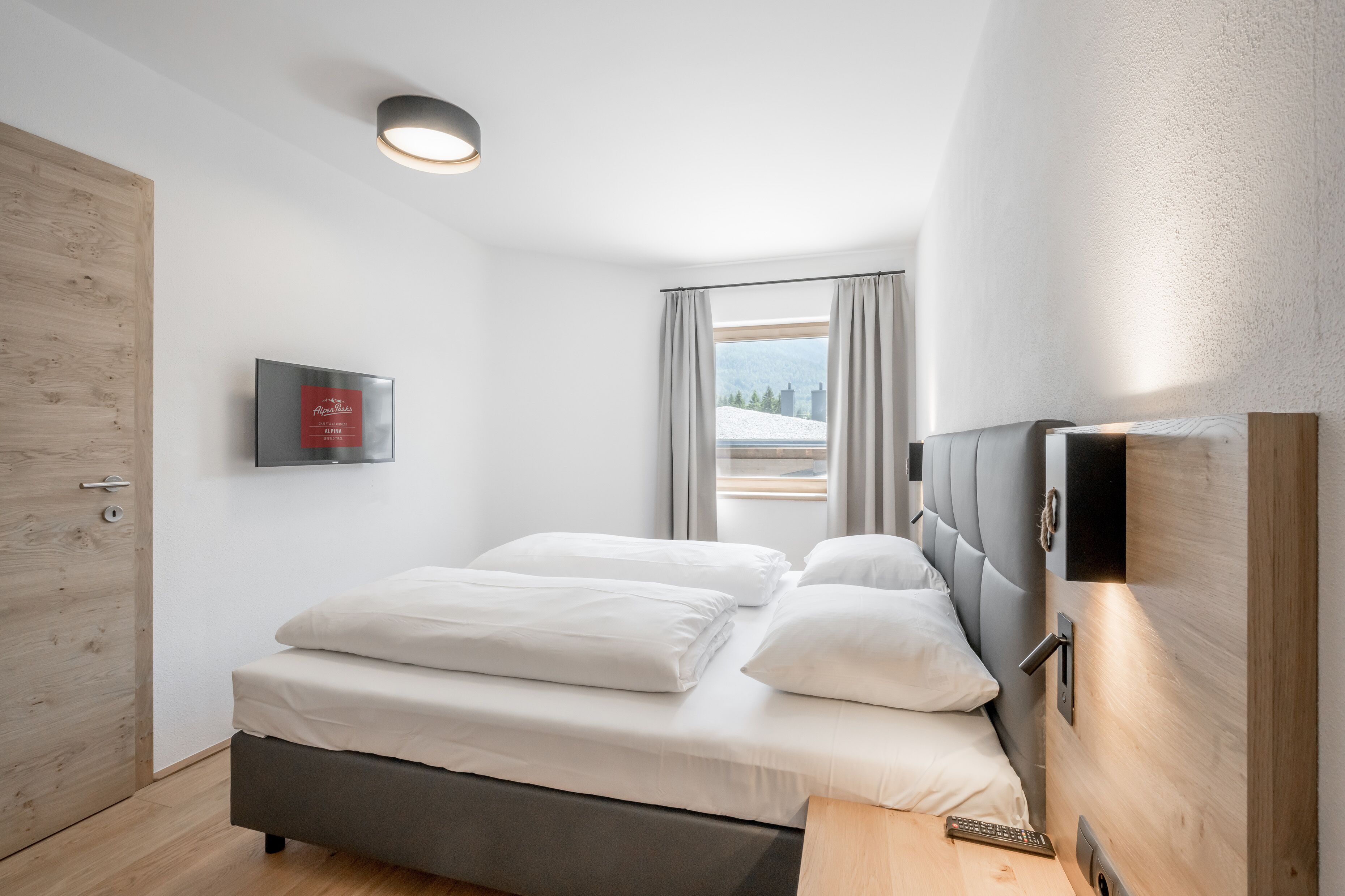 A modern bedroom with a bed, a bedside table, a mounted TV, and a window with curtains.