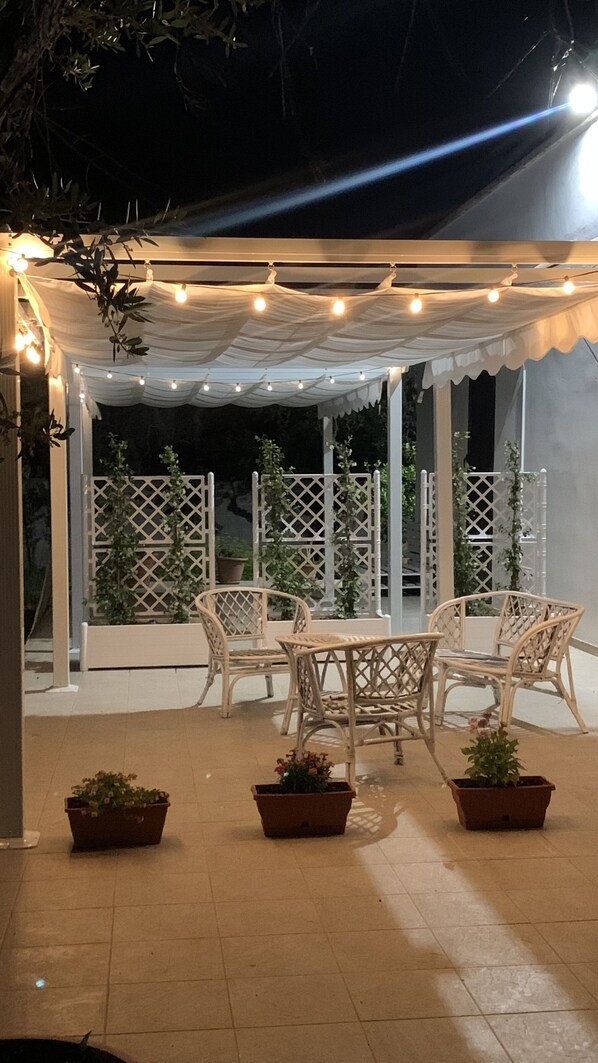 An outdoor patio area with white wicker furniture and potted plants.