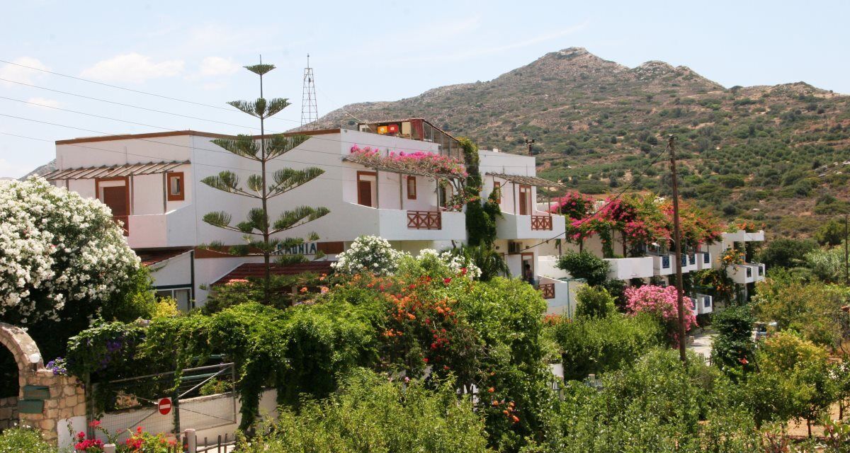 A hillside building with multiple balconies, surrounded by lush greenery and flowering plants.