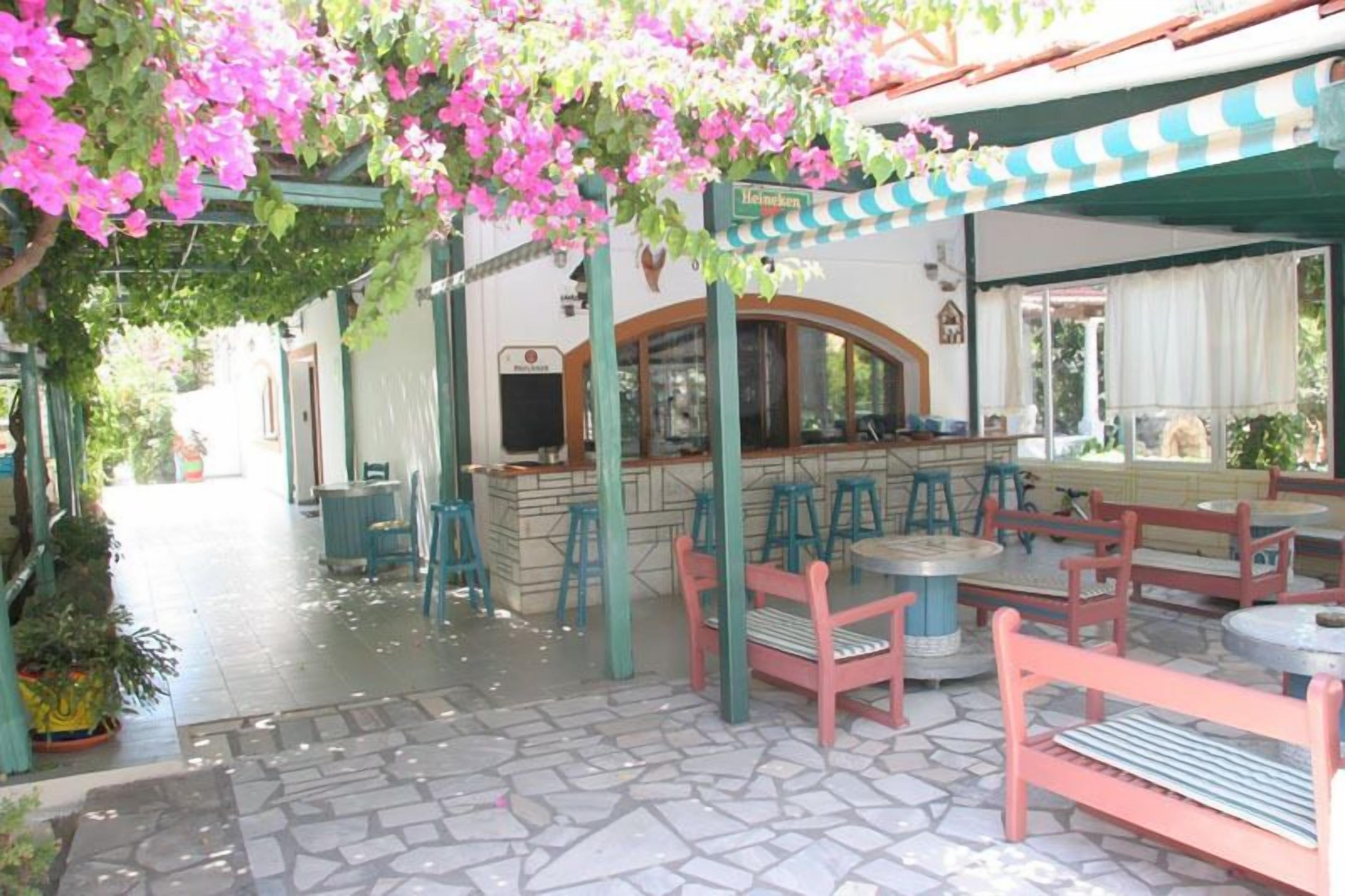 An outdoor café area with stone flooring, wooden and metal furniture, and a Heineken sign.