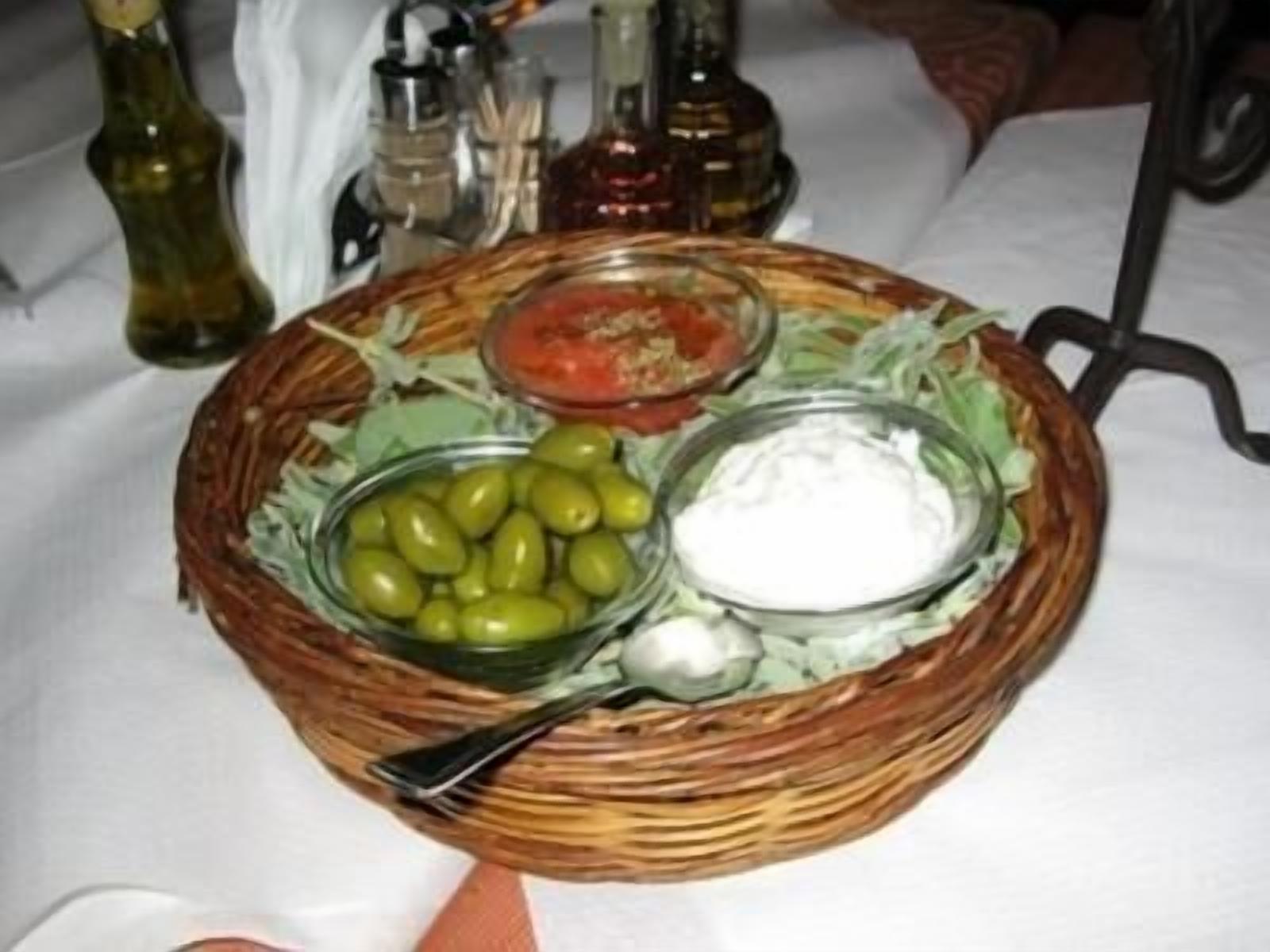 A wicker basket with olives, a bowl of sauce, and a spoon on a table.