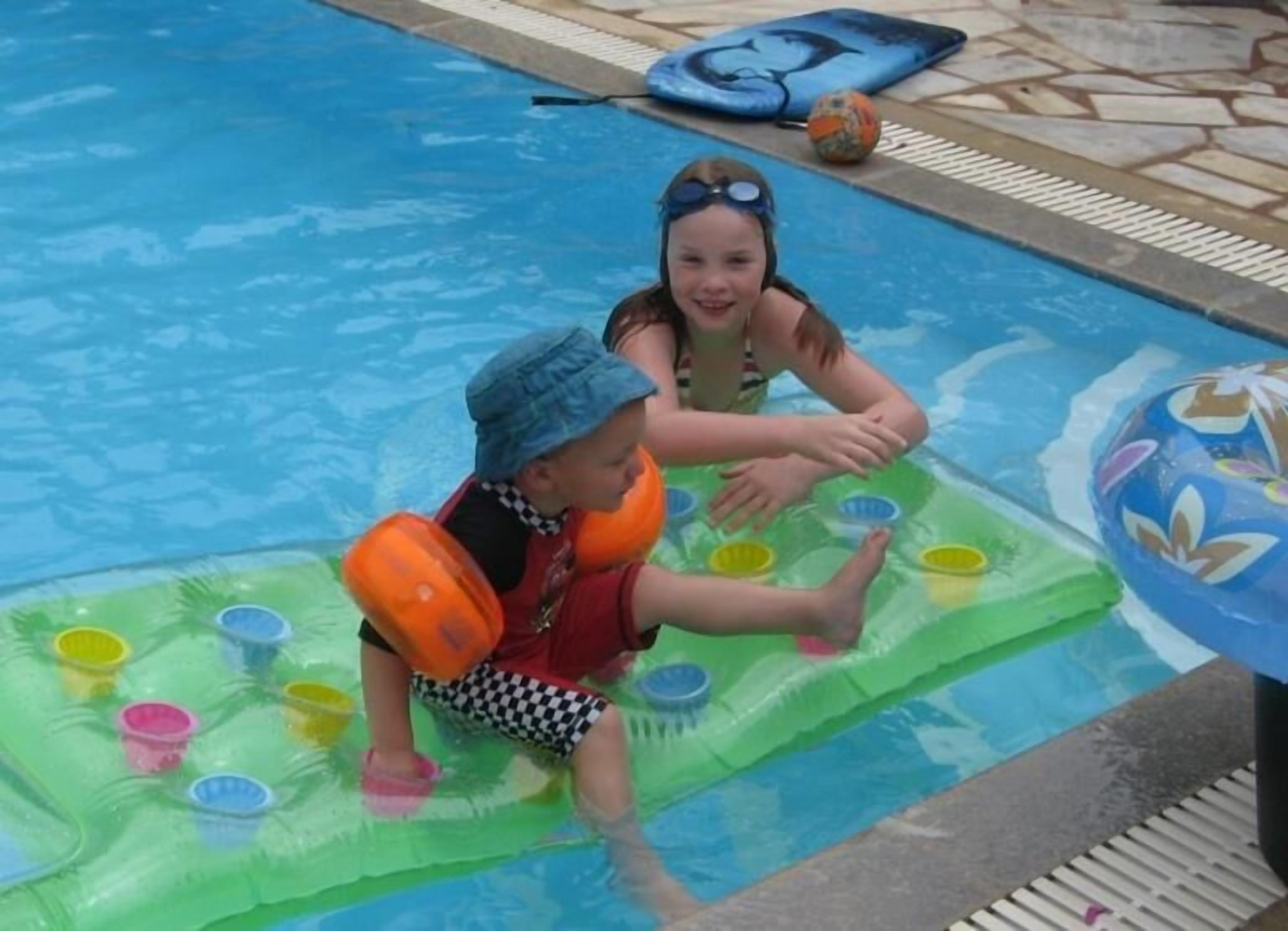 Un espace piscine où deux enfants jouent sur un tapis flottant.