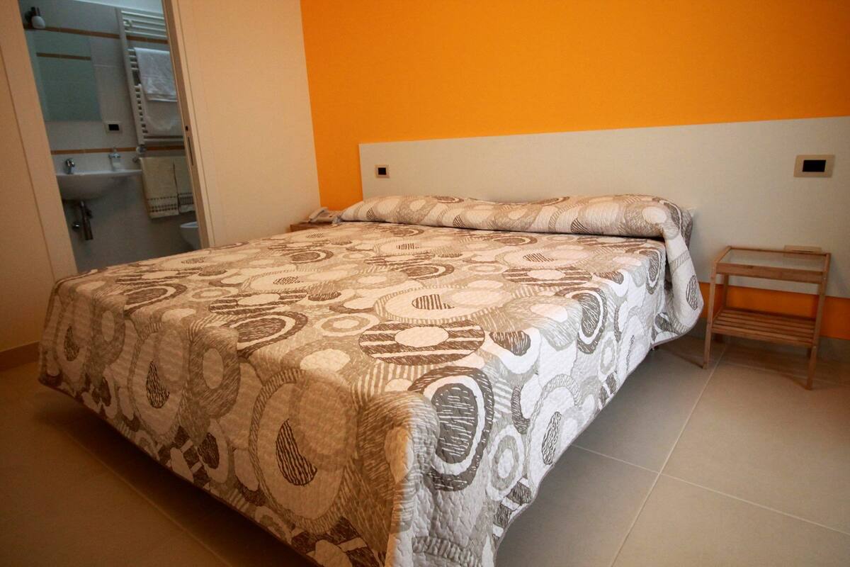 A bedroom with a bed, a nightstand, and a bathroom visible through an open door.