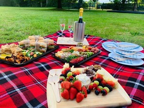 A picnic setup with various food items and a bottle of champagne on a red and black checkered blanket. - The George & Dragon Country Pub & Hotel (Tadley)