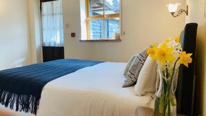 A bedroom with a bed, a window with curtains, a vase with flowers, and a lamp. - The George & Dragon Country Pub & Hotel (Tadley)