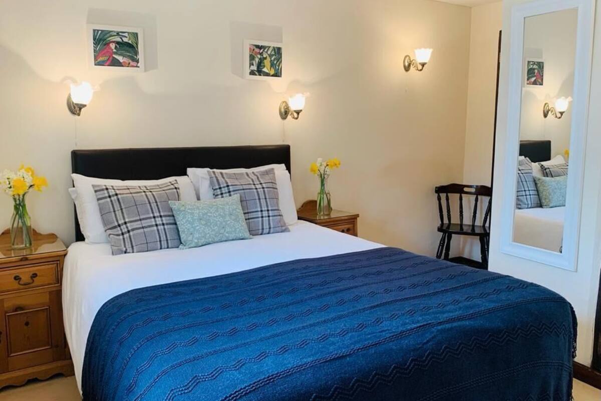 A neatly made bed with a blue patterned bedspread, two wall-mounted light fixtures, and a mirror reflecting the room.