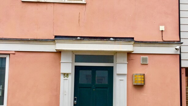 A two-story building with a green door, white-framed windows, and a brick foundation. - Home away from Home (Colchester)