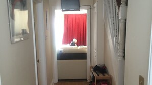A narrow hallway with a wooden floor, a radiator, a red curtain, and a staircase with white balusters. - Home away from Home (Colchester)