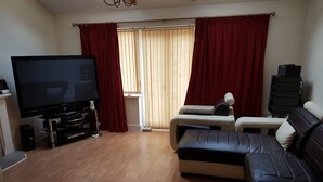 A living room with a flat-screen TV, a sofa, a chair, and a small table. - Home away from Home (Colchester)
