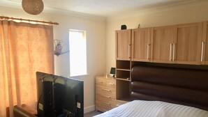 A bedroom with a bed, a TV, a dresser, and a window. - Home away from Home (Colchester)