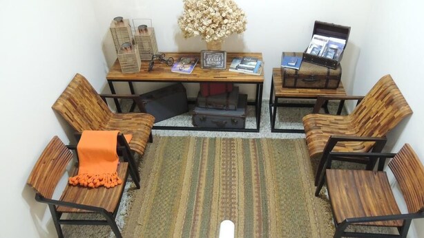 Une pièce comprenant un bureau en bois, deux chaises, une petite table, un vase avec des fleurs séchées et un écran d’ordinateur.
