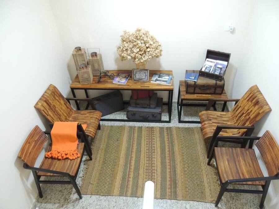 A room with a wooden desk, two chairs, a small table, a vase with dried flowers, and a computer monitor.