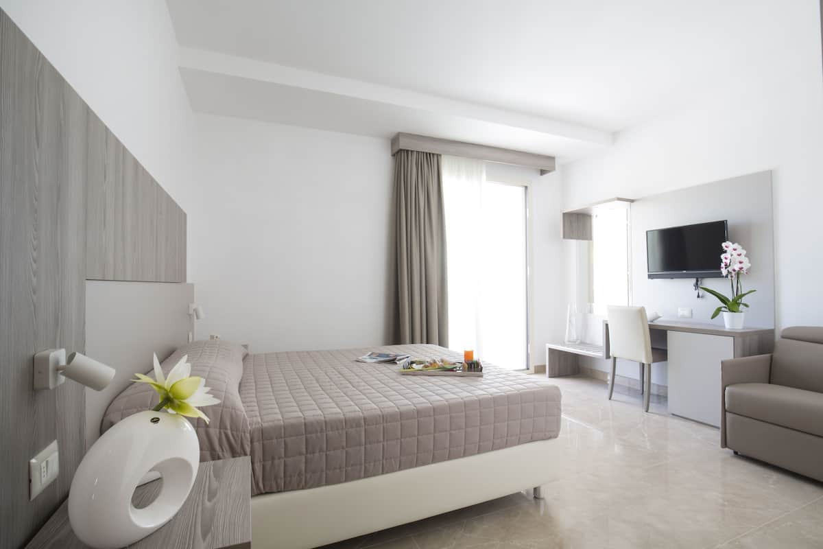 A modern hotel room with a bed, a desk, a TV, and a bathroom.